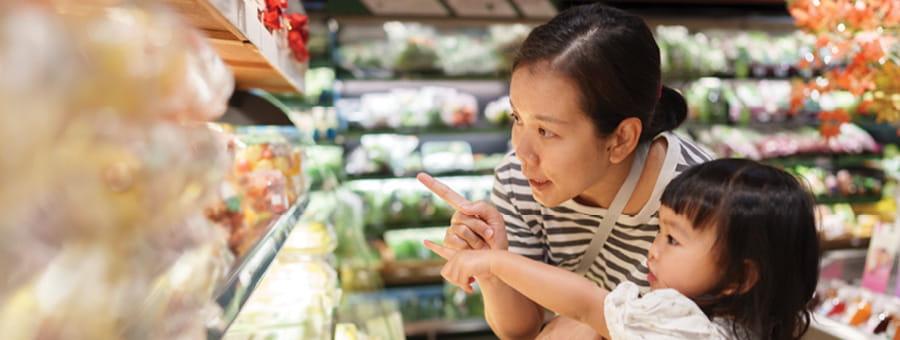 A mother and child point toward produce at a grocery store.