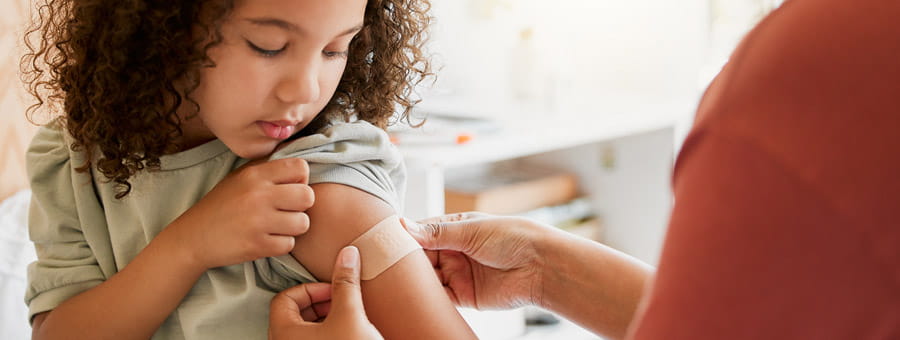 Adult helps child apply bandage to arm.