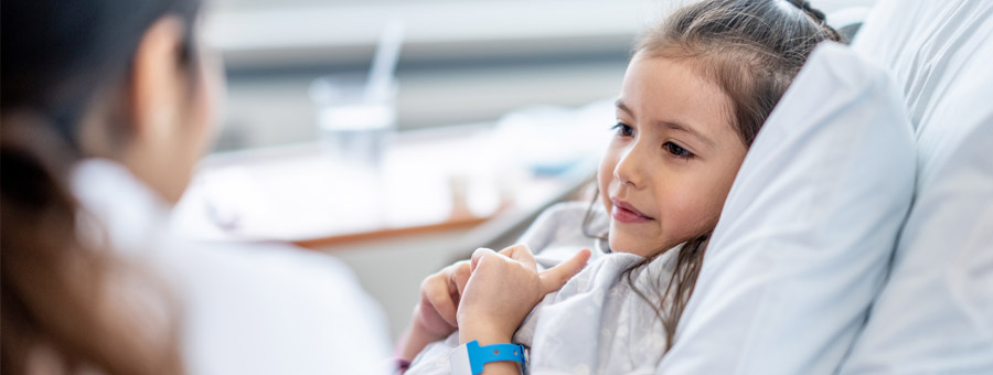 Girl in hospital bed looks at doctor.