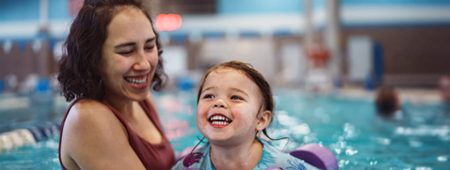 Woman helps child swim in pool.