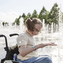 Happy girl in wheelchair at splash park fountain.