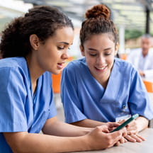 Two nurses talking and looking at mobile phone.