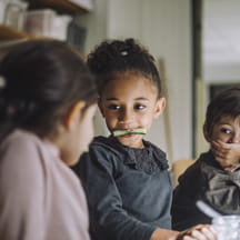 Kids joking around, eating a dinner with vegetables.